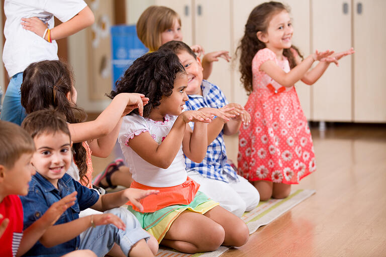 Group of children sitting and standing around clapping hands and dancing