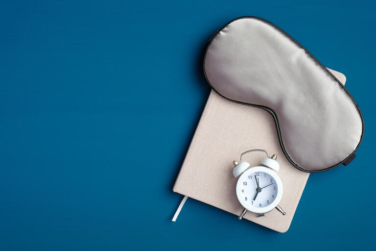 Flat lay composition with sleep eye mask, dream book and alarm clock on dark blue background. Healthy sleeping concept.