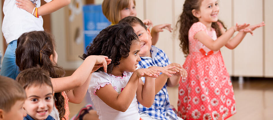 Group of children sitting and standing around clapping hands and dancing