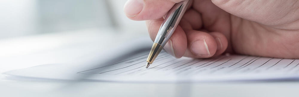 Image of hand signing paperwork with pen