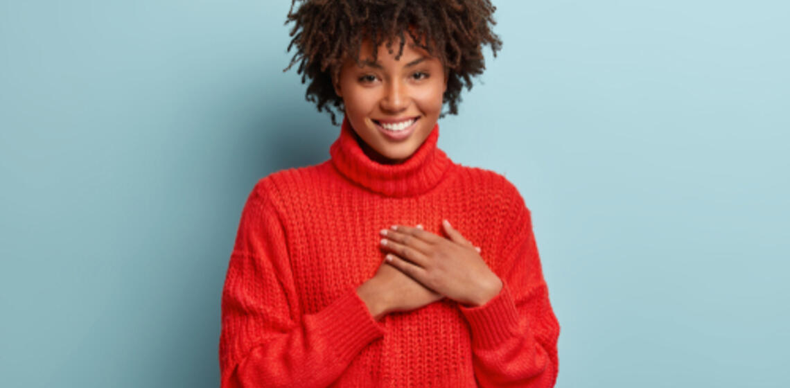 A smiling person holds their hands over their heart