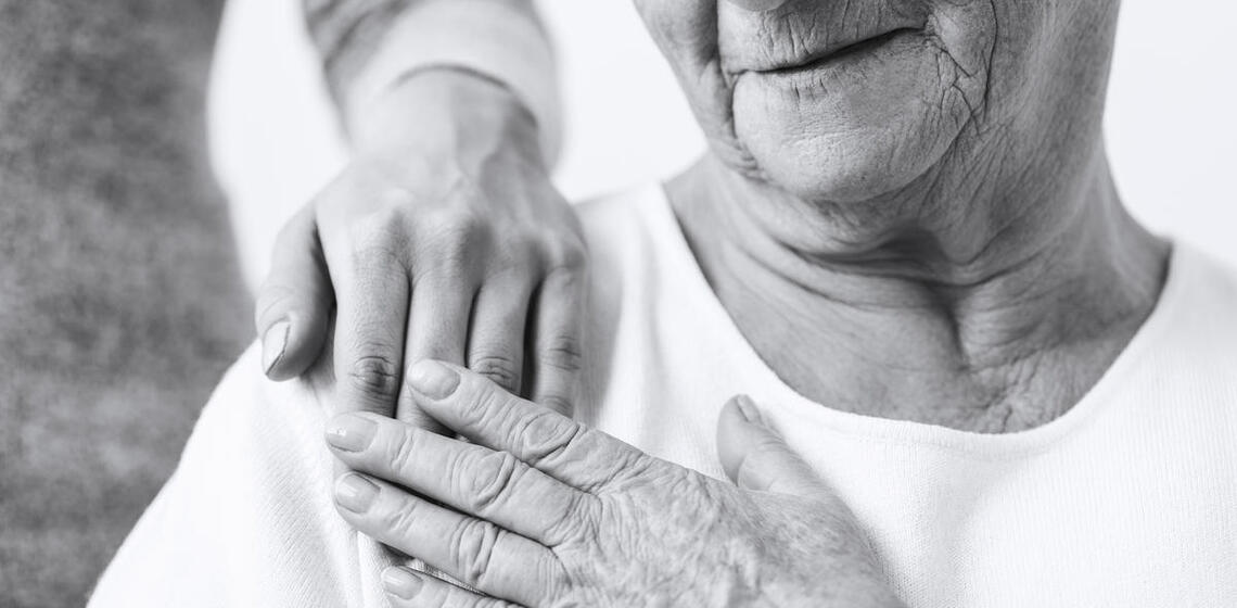 Black and white photo of elderly person, a caregiver's hand on their shoulder