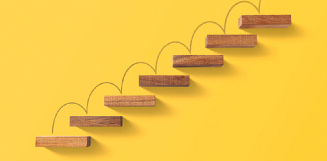 Wooden blocks arranged in a shape of staircase on yellow background.
