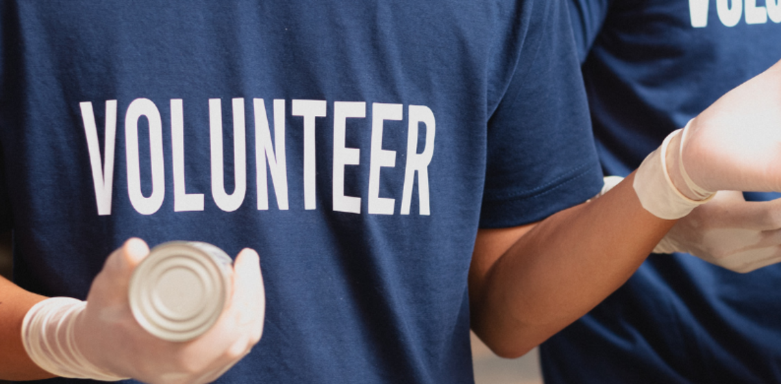 A person wearing a Volunteer tshirt hands out canned goods.