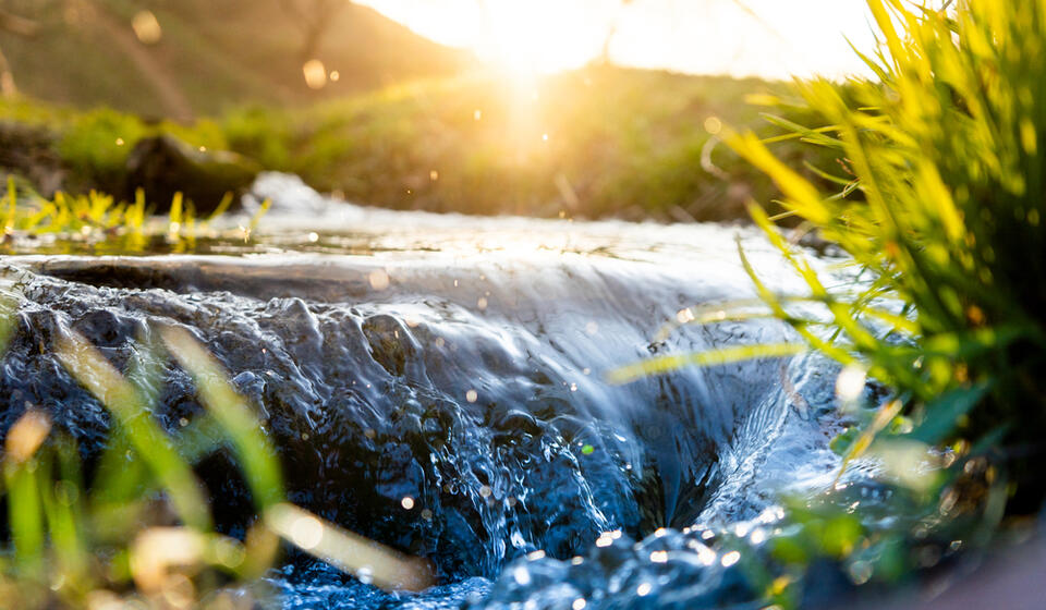 A river flows over rocks creating a waterfall with the sun rising in the background