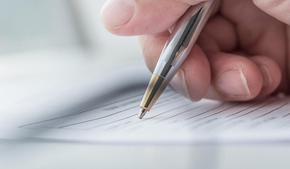 A hand holding a silver pen signing a document