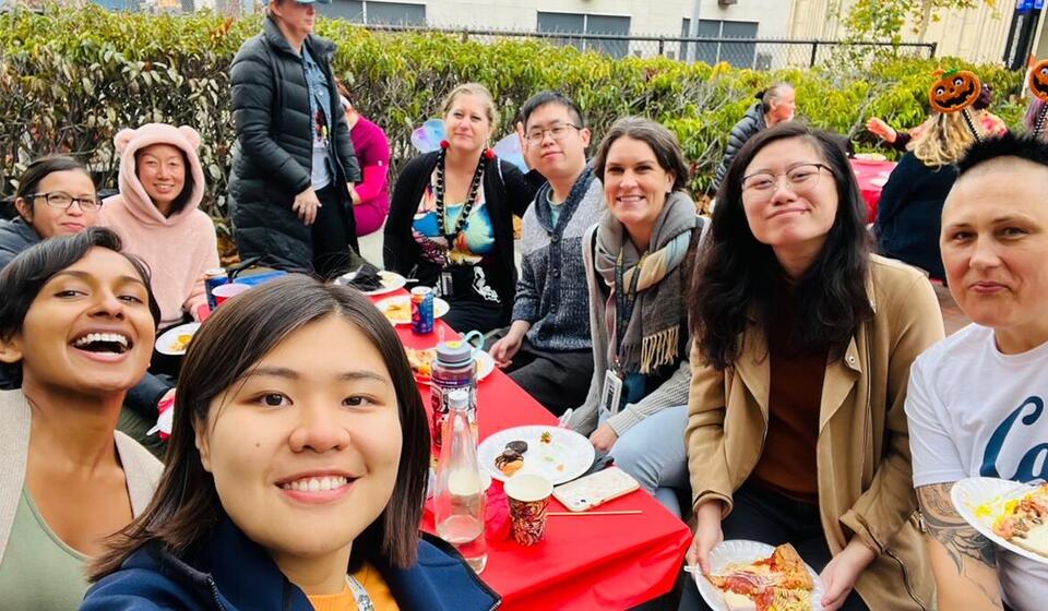 Selfie of Trainees and Staff outdoors enjoying pizza at a potluck lunch