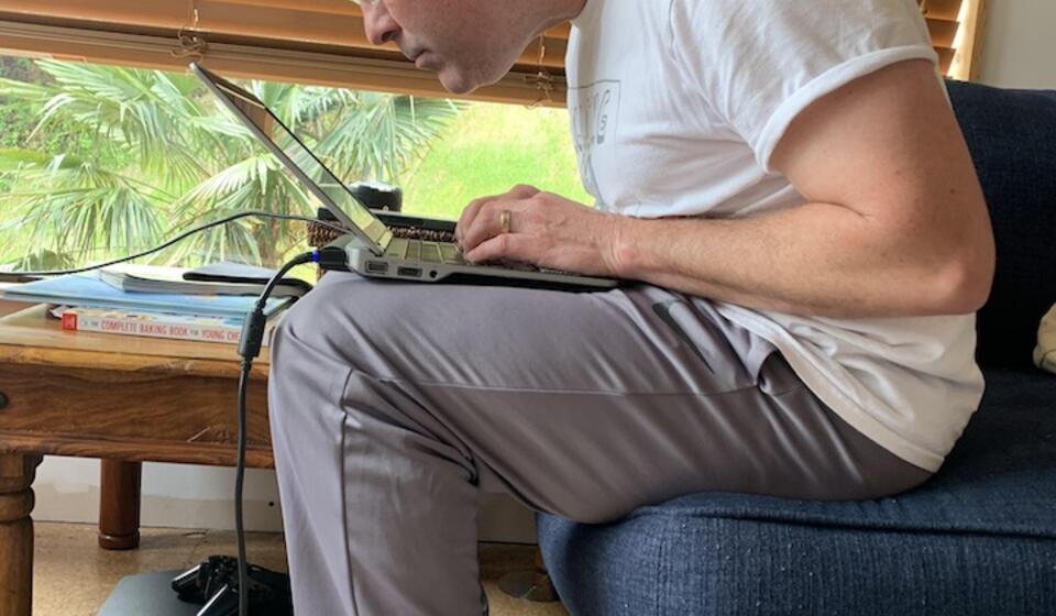 Person sits with a laptop on their lap. Their posture creates a strain in the back
