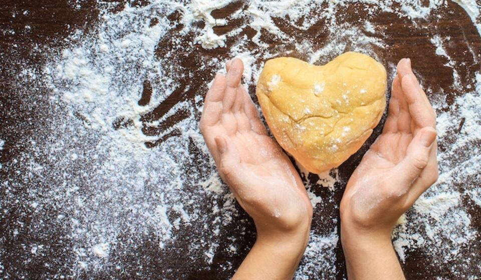 A person kneads dough into a heart shape on a flour laden worktop