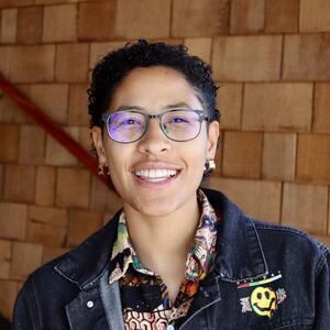 A professional headshot of a person smiling wearing glasses